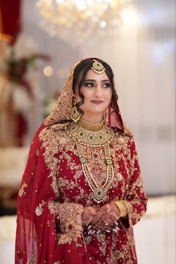 Bride in a red embroidered outfit with traditional gold and green jewellery